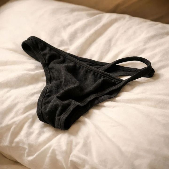 Worn black cotton thong lying on a bed