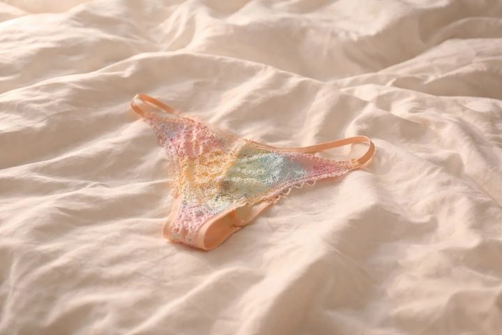 Worn pastel lace thong lying on a sheet